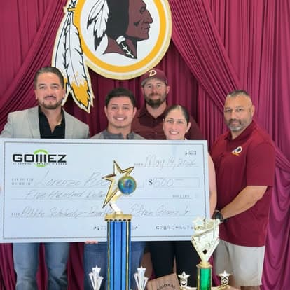 Efrain Gomez Jr. with community members presenting an oversized Gomez Construction scholarship check beside student trophies