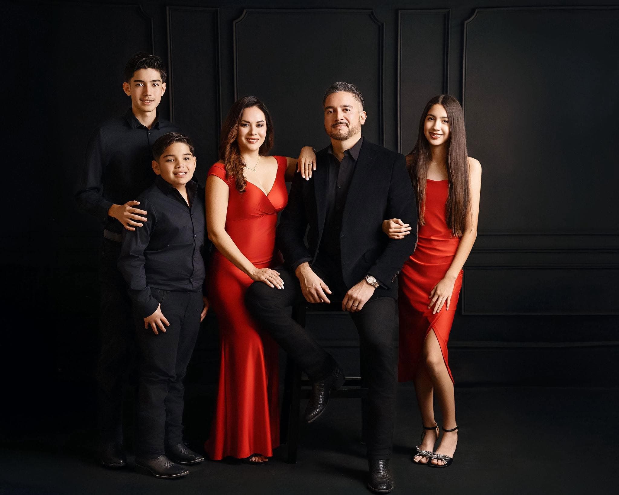 Efrain Gomez Jr. with his family, dressed in black and red, in a formal studio portrait