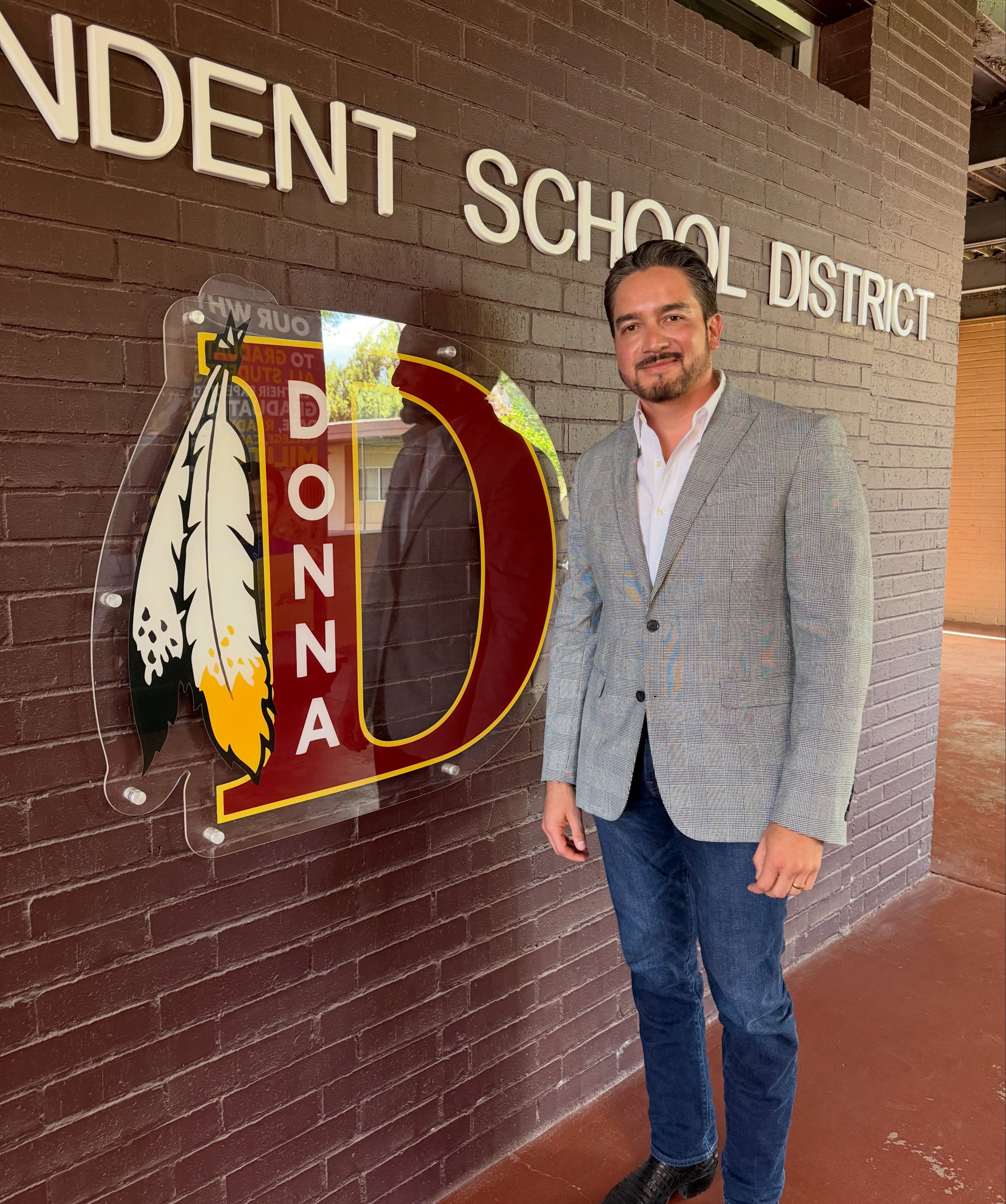 Efrain Gomez Jr. standing next to a brick wall with the Donna Independent School District lettering and the Donna D emblem